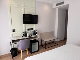 A hotel room with a bed, a desk with a chair, a television, a coffee maker, a mini-fridge, and a trash bin.