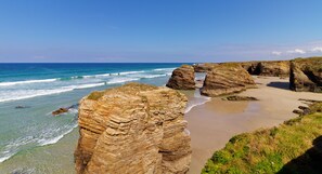 A coastal landscape with layered rock formations and a sandy beach. - Playa de Foz Hotel & Spa by gaiarooms (Foz)