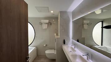 Une salle de bain moderne avec un grand miroir, deux lavabos, des toilettes et une baignoire.