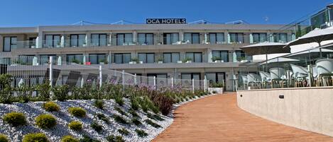 Un hotel de diseño moderno, con un llamativo letrero 'OCA HOTELS' y un espacio exterior bien cuidado que incluye un camino y un jardín ajardinado.