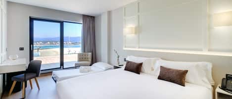 A hotel room with a large bed, a desk, a chair, and a view of the beach.