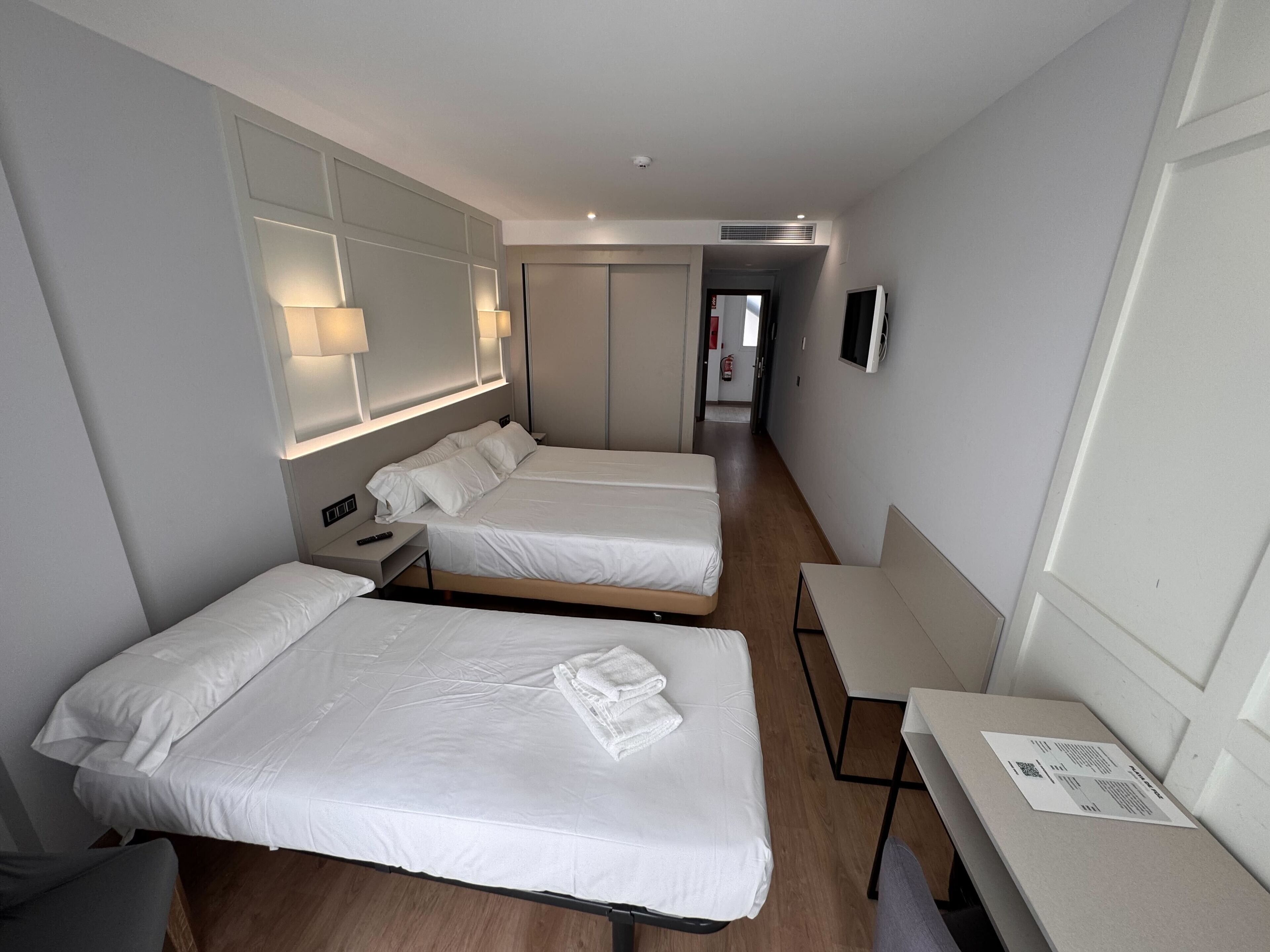 Ein Hotelzimmer mit zwei Einzelbetten, einem Schreibtisch, einem Stuhl, einem Fernseher und einem Kleiderschrank.