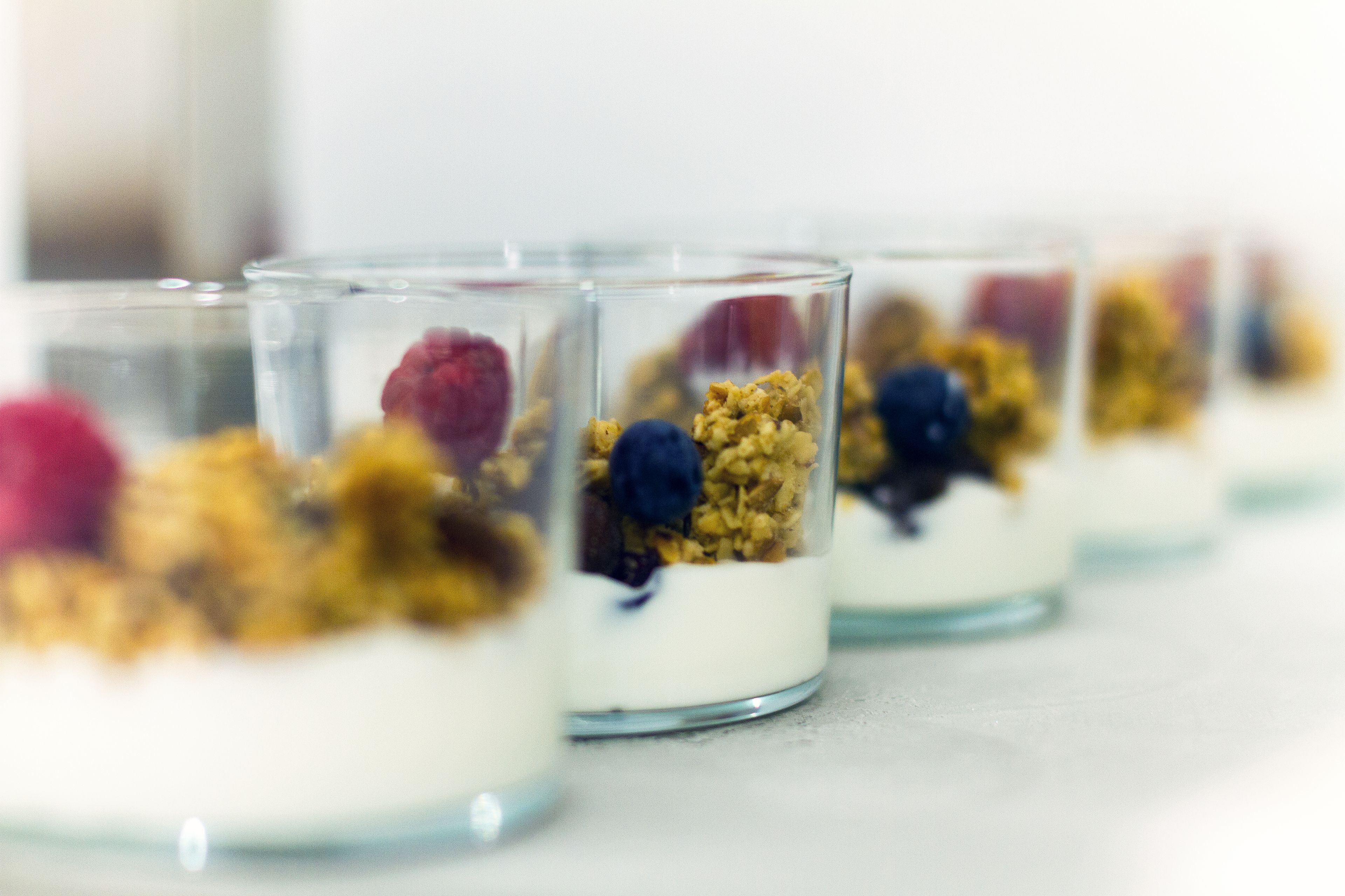 A row of clear glass dessert cups with layers of yogurt, granola, and berries.