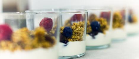 A row of clear glass dessert cups with layers of yogurt, granola, and berries.
