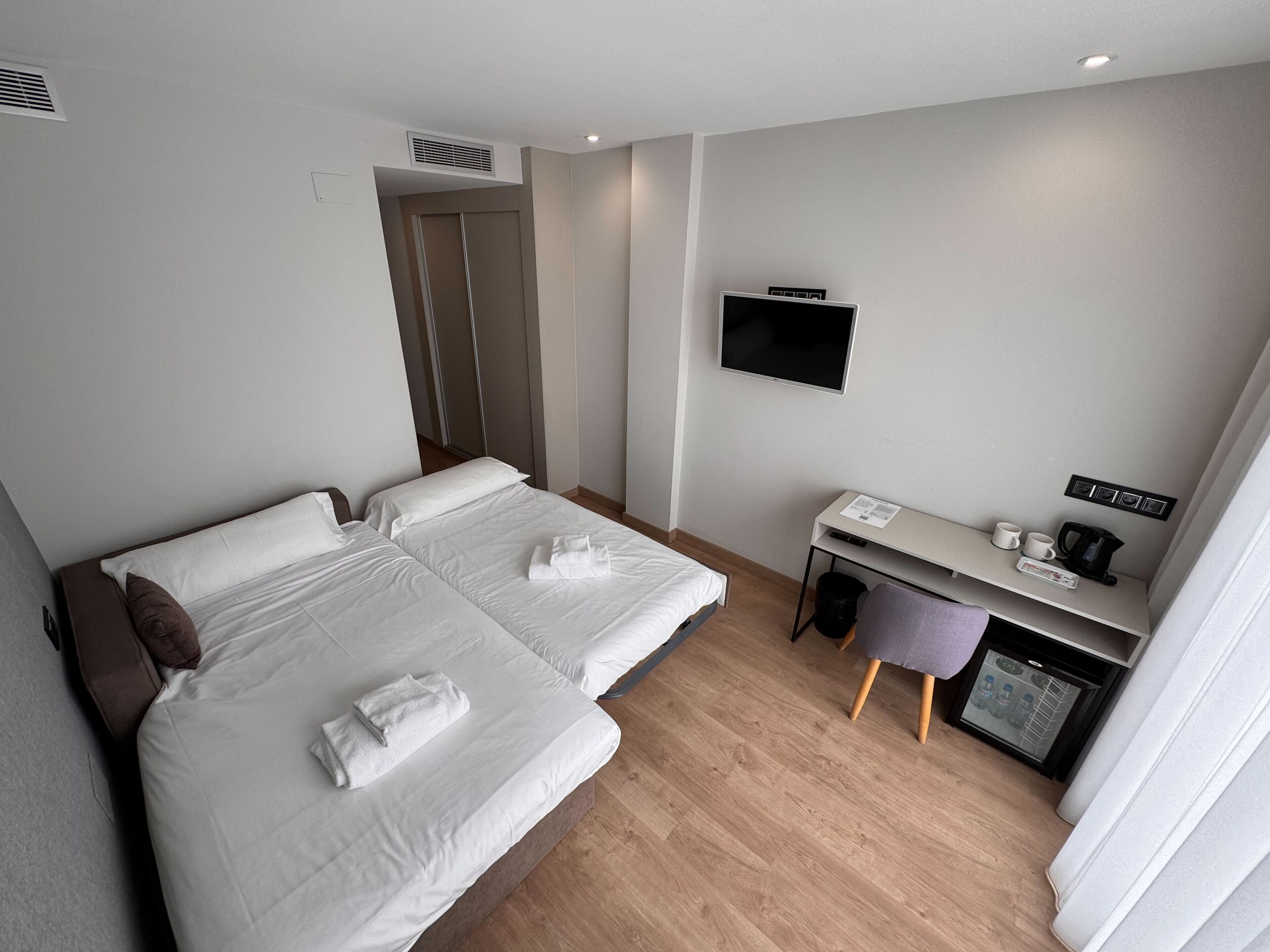 Una habitación de hotel con dos camas, un escritorio con computadora, televisor y una pequeña kitchenette.