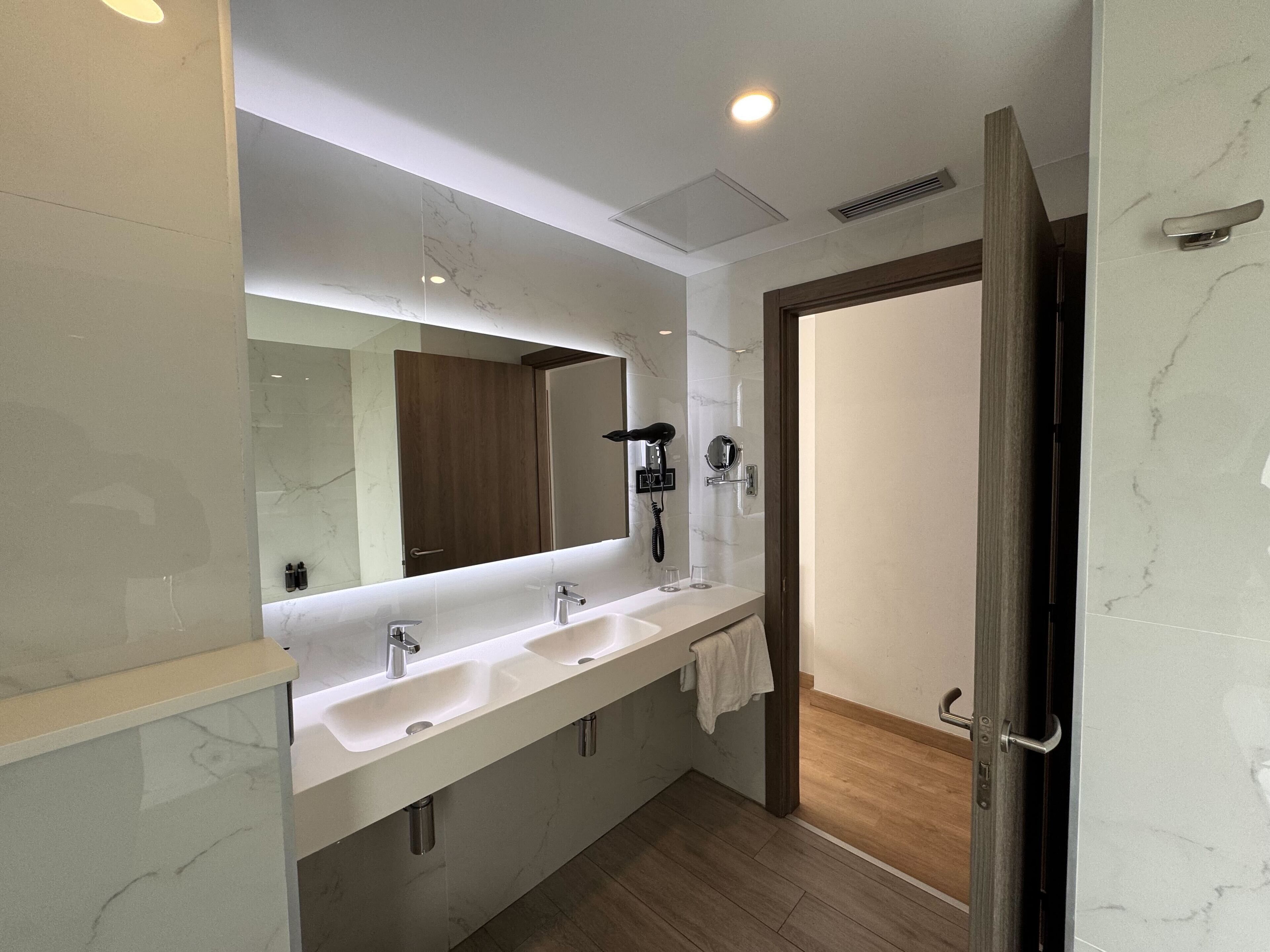 Un baño moderno con dos lavamanos, un espejo grande, un secador de pelo y un perchero para toallas.