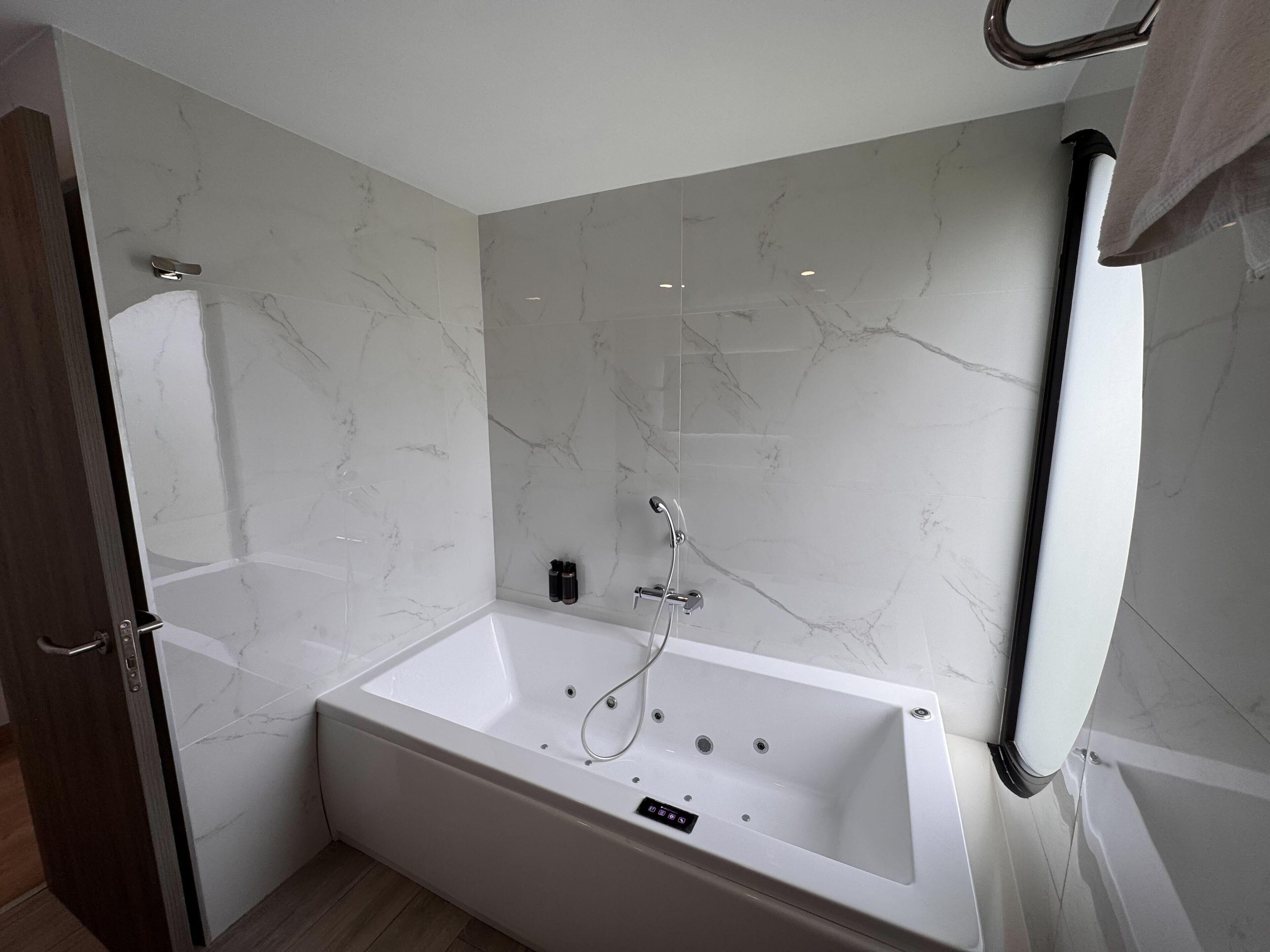 Un baño moderno con una bañera blanca grande, paredes de mármol y suelo de madera.
