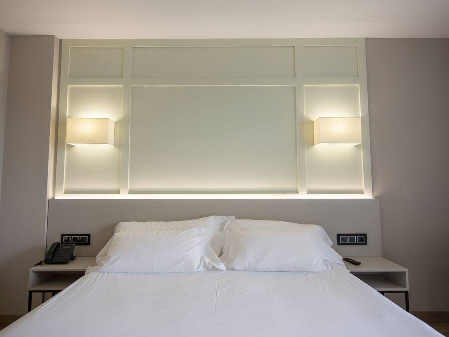 Een hotelkamer met een groot bed, twee nachtkastjes, een stoel en een wandlamp.