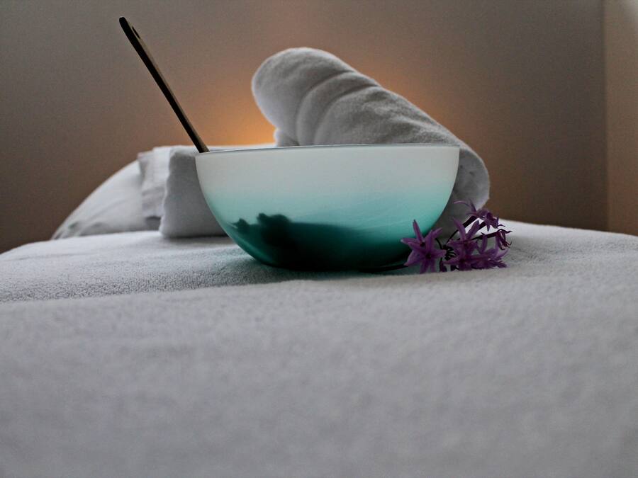 A bowl with a straw, a towel, and a purple flower on a white surface.