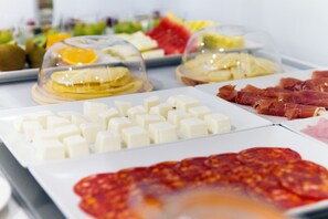 Un bufé con diversas opciones de comida, incluyendo queso, embutidos y frutas.
