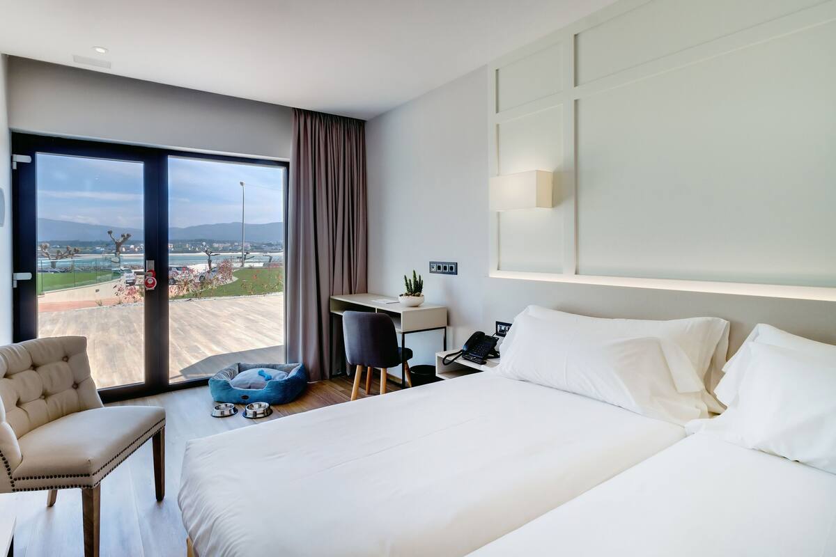 A hotel room with a large bed, a desk, a chair, and a view of a cityscape.