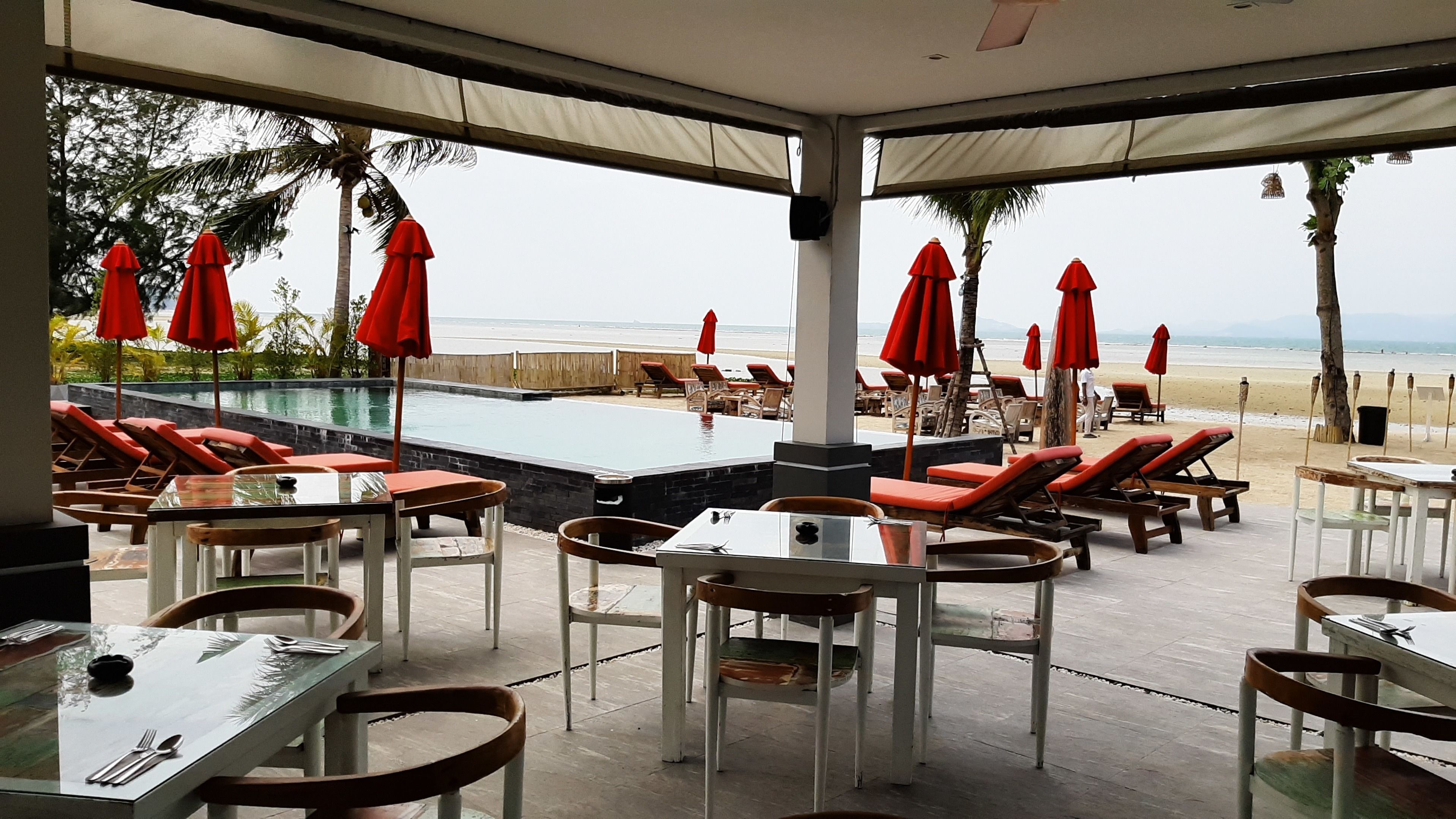 A poolside area with lounge chairs and tables, a pool, and a view of the beach.