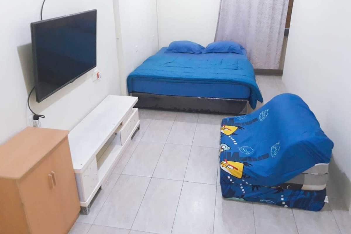 Ein kleiner, sauberer Raum mit einem Bett, einem Fernseher, einem Schrank und einem abgedeckten Sessel.