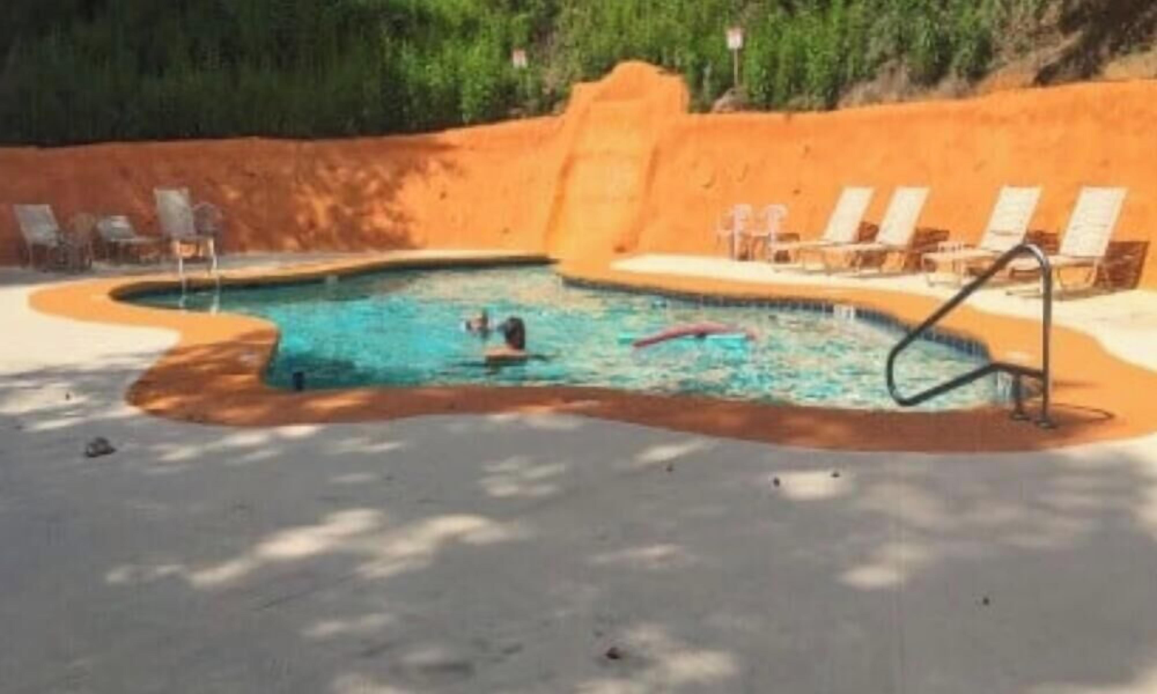 A swimming pool with a sandy border, surrounded by lounge chairs and a shaded area.