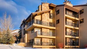 Un immeuble à plusieurs étages doté de balcons, d’une façade en pierre et situé dans un environnement enneigé.