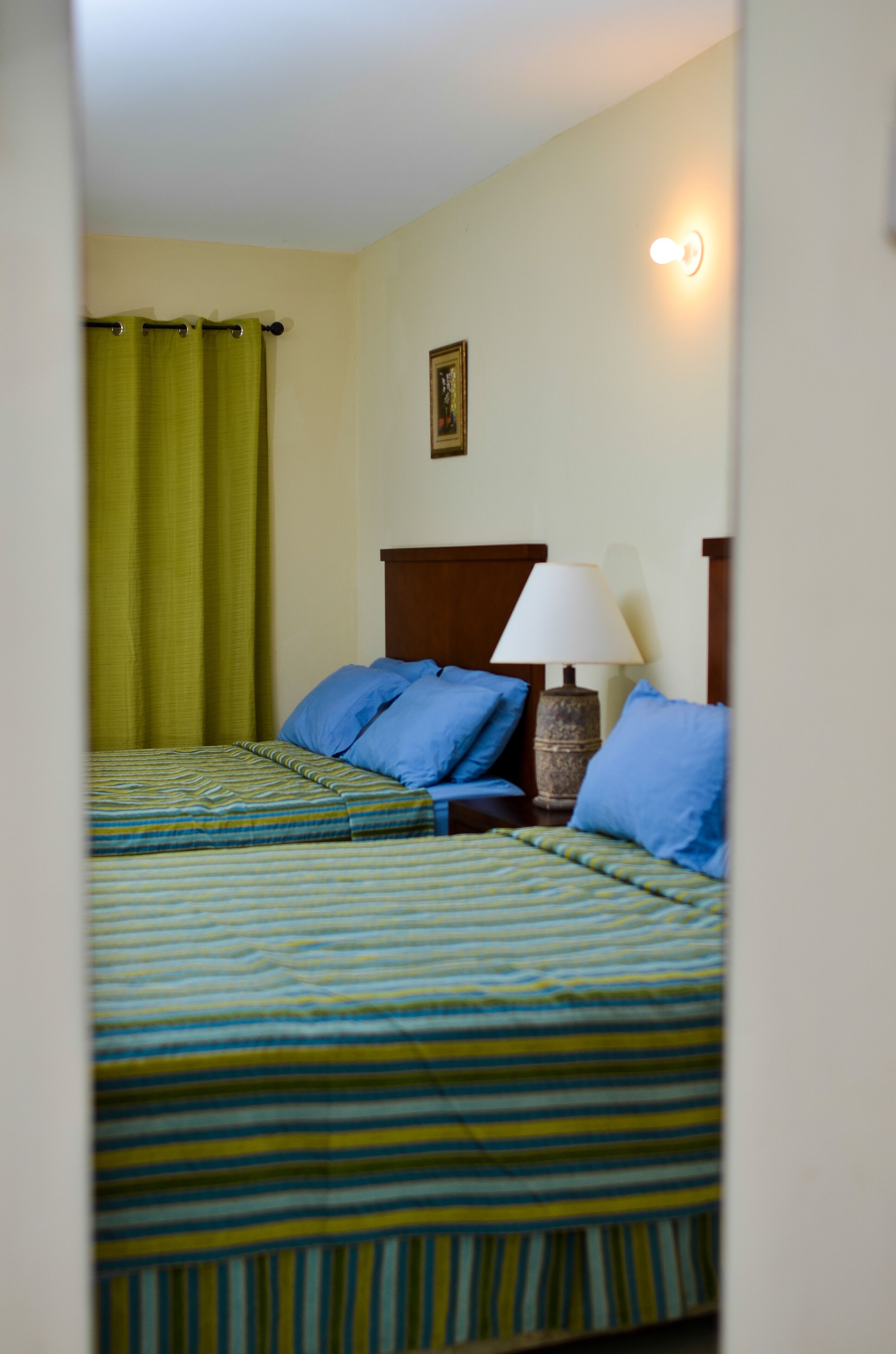 A hotel room with a bed, a nightstand, a lamp, and a green curtain.
