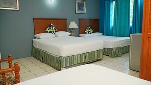 Ein Hotelzimmer mit zwei Betten, einem Holzkopfende, gestreifter Bettdecke, einem Nachttisch mit Lampe und einem kleinen Tisch.