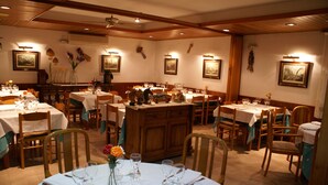 A restaurant with multiple dining tables, chairs, and wall-mounted artwork. - Hotel Edelweiss (Naut Aran)