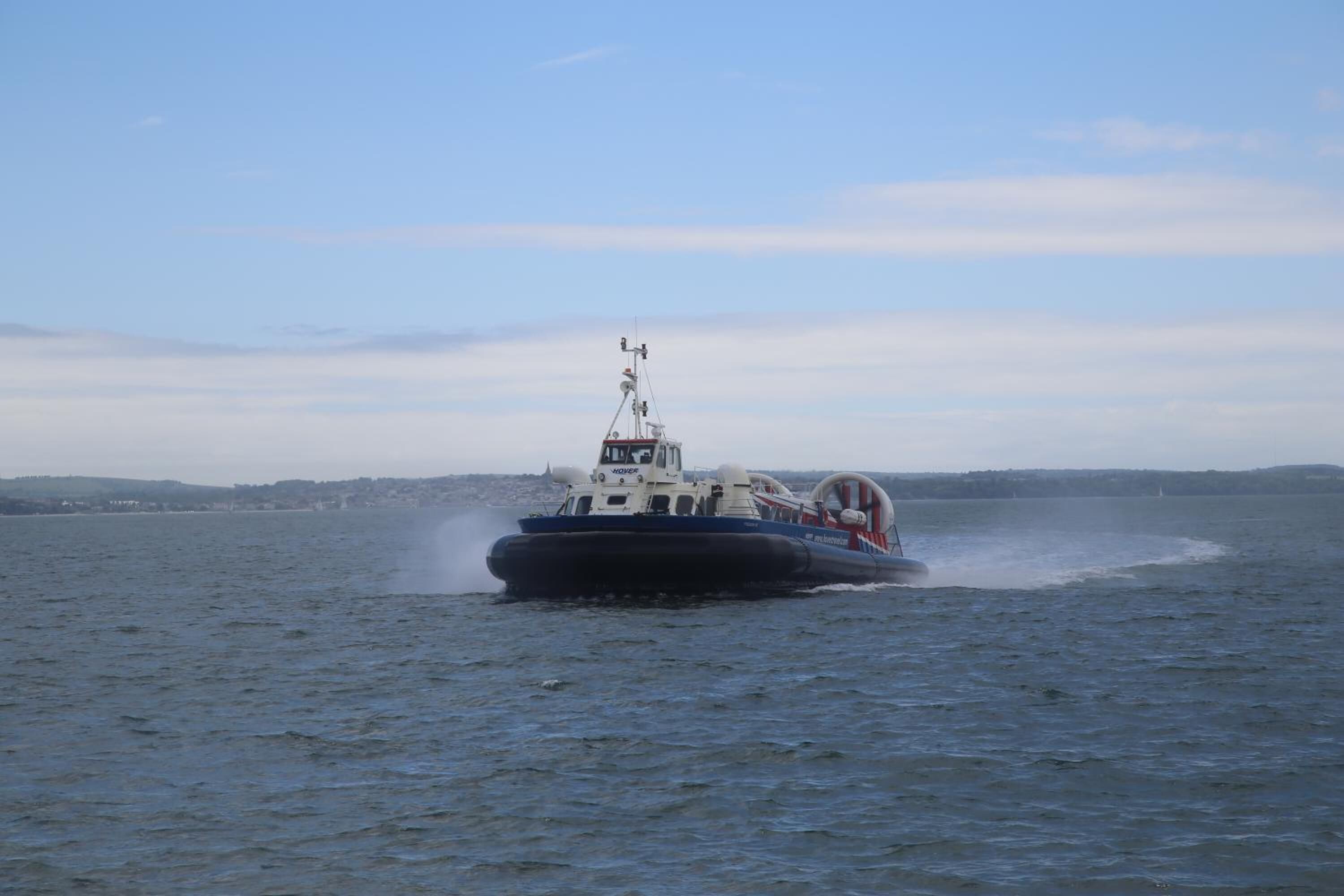 A boat moving through a body of water with a distant shoreline in the background.