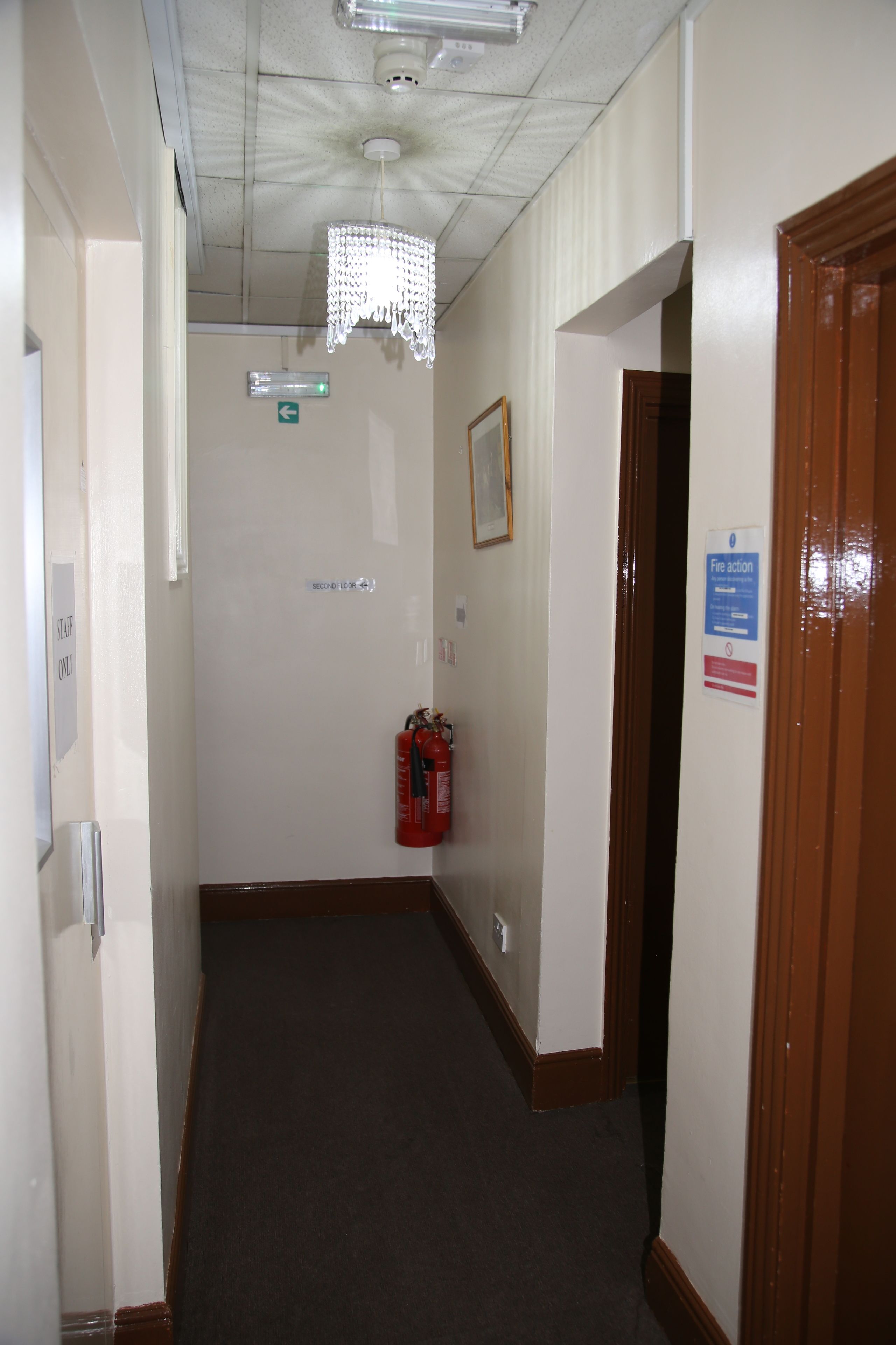 A hallway with a fire extinguisher, a sign indicating a fire action procedure, and a door with a sign that says "Fire action only".