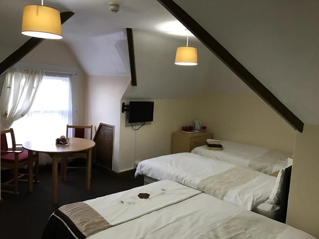 A room with two beds, a table, chairs, a television, and a window with curtains.