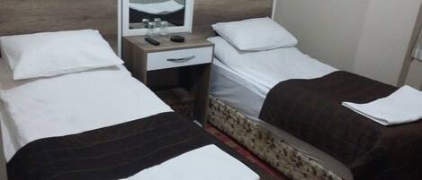 A hotel room with two single beds, a small bedside table with a lamp, a mirror, and a nightstand with a remote control.
