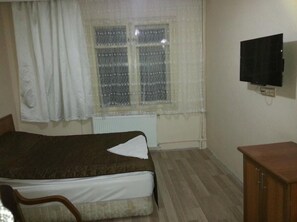 A bedroom with a bed, a window with curtains, a radiator, a television on the wall, and a wooden cabinet. - Hotel Kervansaray (Erzurum)