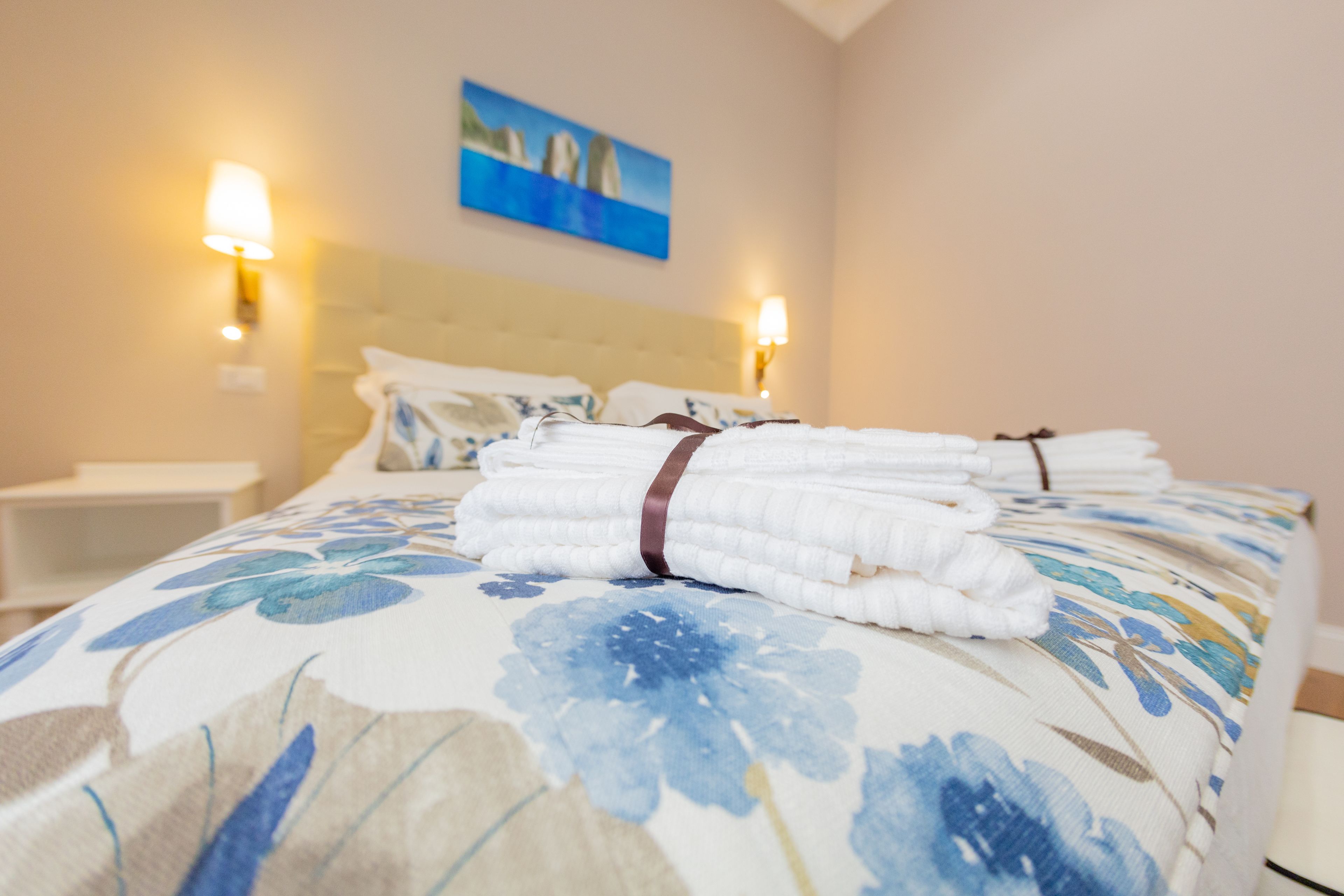 A neatly made bed with folded towels and a floral-patterned bedspread.