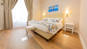Un dormitorio con cama, mesitas de noche, una ventana con cortinas y un cuadro en la pared.