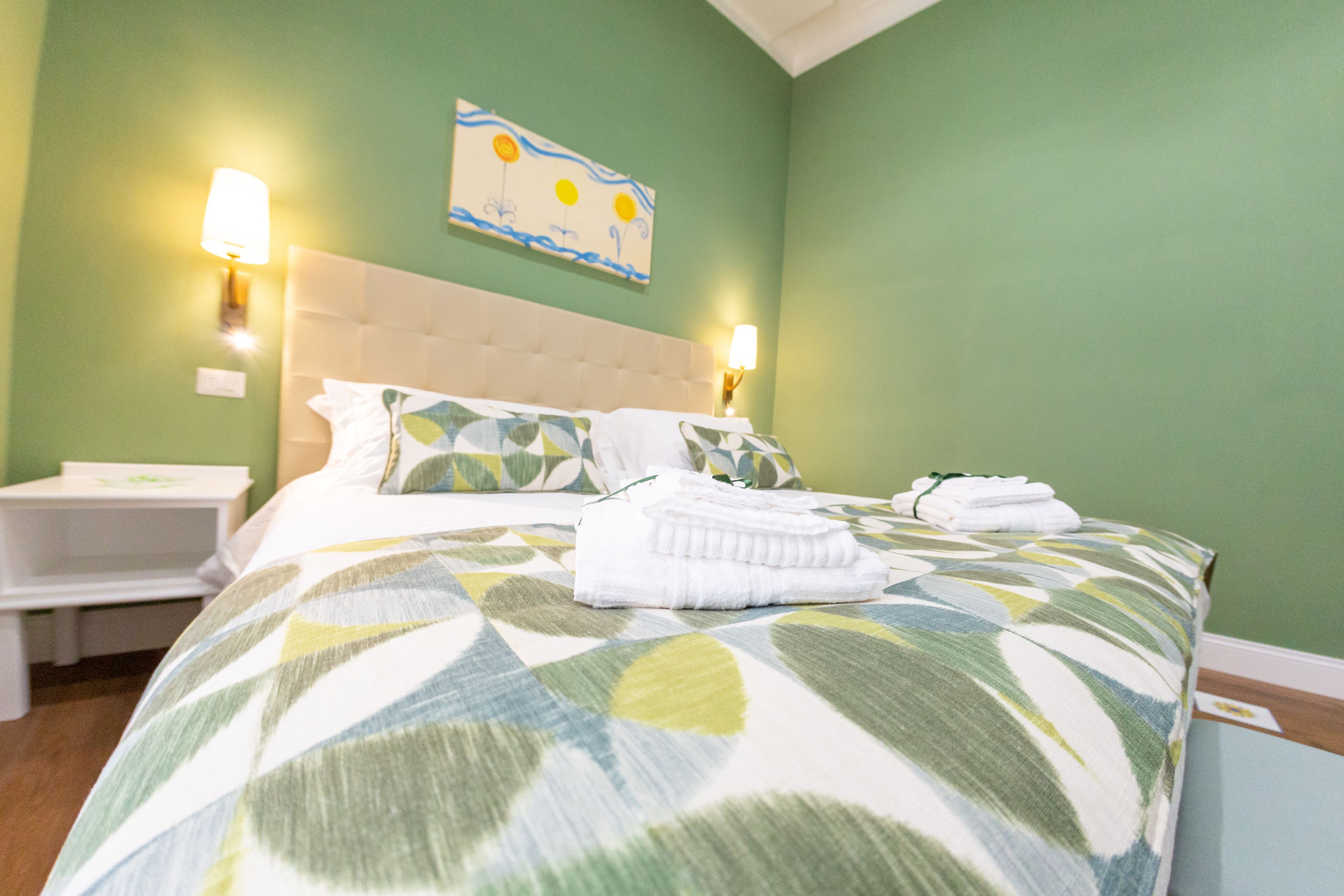 Een net opgemaakt bed met een bedsprei met patroon, twee bedlampen, een nachtkastje en een schilderij aan de muur.