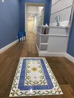 Een hal met een vloerkleed met patroon, een wit wandrek en een blauwe muur.
