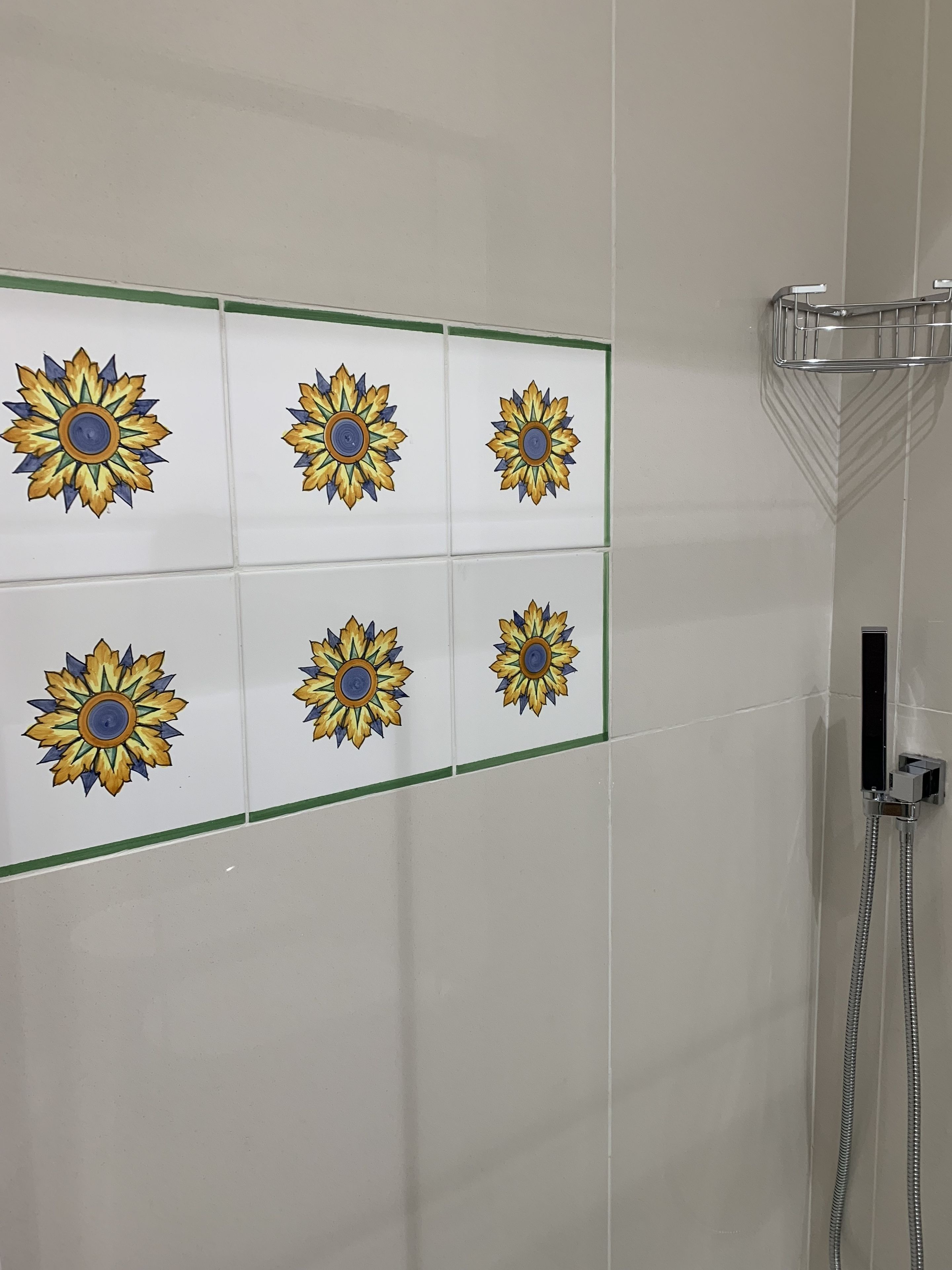 Zona de ducha con mampara de vidrio y pared revestida de azulejos con diseño de girasoles.