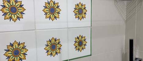 Zona de ducha con mampara de vidrio y pared revestida de azulejos con diseño de girasoles.