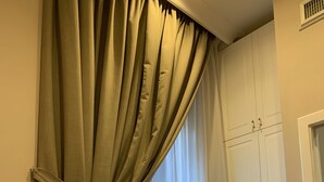 Una habitación con un ventanal grande cubierto por cortinas color beige, suelo de madera y armarios empotrados blancos.