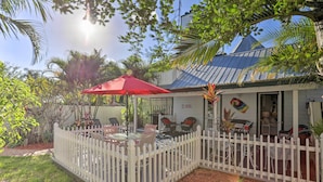 A covered patio with outdoor seating, a white picket fence, and tropical plants. - Stuart Apartment w/ Patio Near St Lucie River! (Stuart)