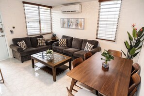 Una sala de estar con sofá, una mesa de centro, una mesa de comedor y una planta en maceta.