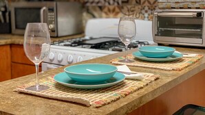 A kitchen with a gas stove, microwave, and toaster oven. There are two turquoise plates and two wine glasses on the counter.