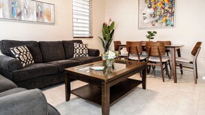A living room with a sofa, coffee table, and dining area with chairs.