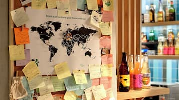 Un tablón de corcho con notas y un mapa del mundo, una barra de madera y una zona de bar con botellas.