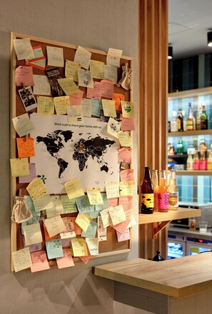 A corkboard with pinned notes and a world map, a wooden counter, and a bar area with bottles. - Hotel Traffic Wrocław Stare Miasto (Wroclaw)
