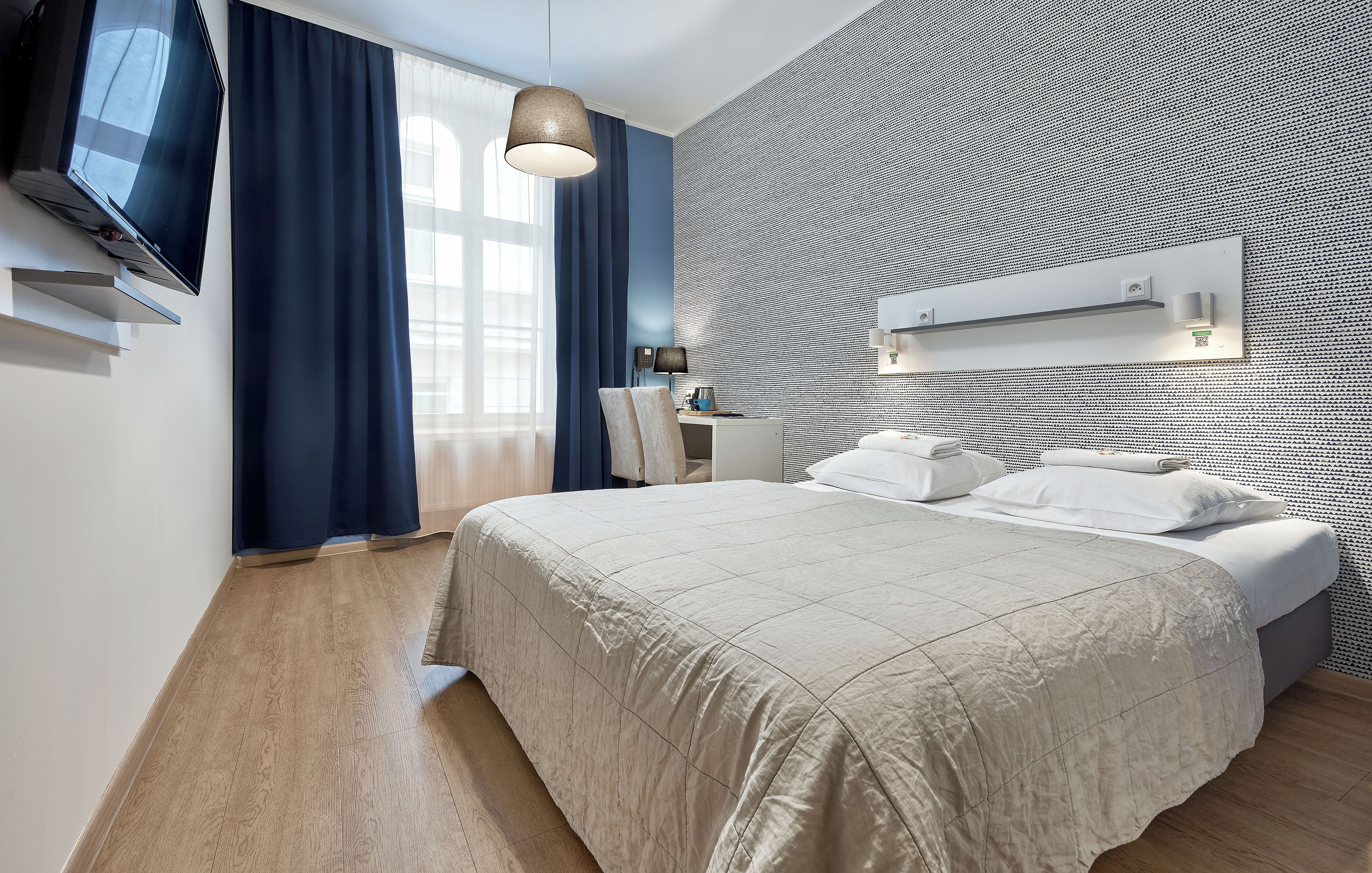 Camera d'albergo moderna con un letto, una scrivania, una sedia, una TV e una parete decorata.