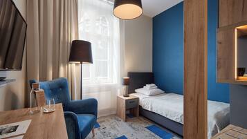 A hotel room with a bed, a chair, a table, a lamp, and a window with curtains.