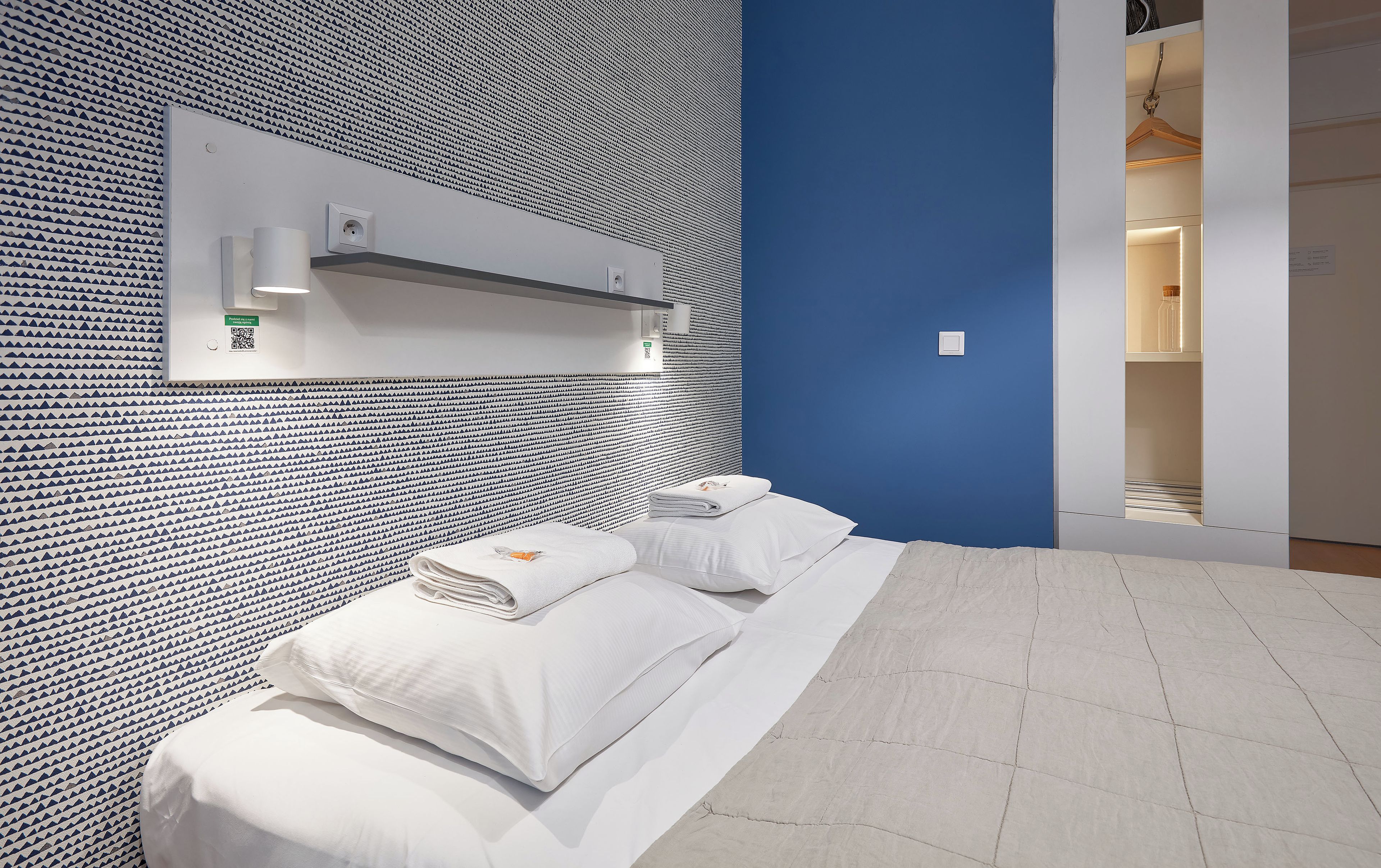 A hotel room with a patterned wall, a bed with white linens, and a blue accent wall.