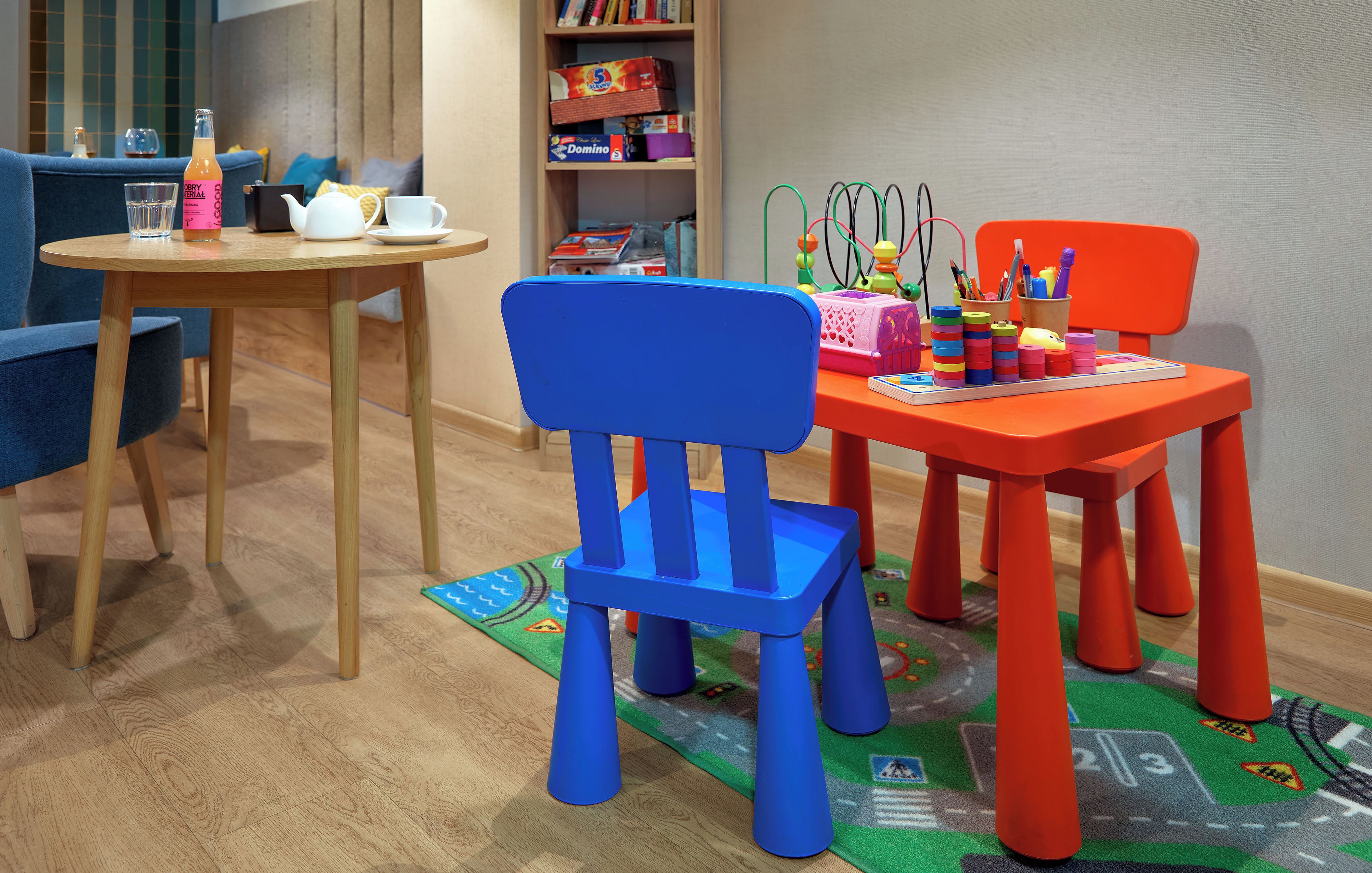 A room with a round wooden table, a blue chair, and a red chair with toys and books.