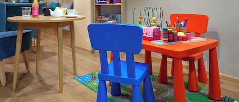 A room with a round wooden table, a blue chair, and a red chair with toys and books.