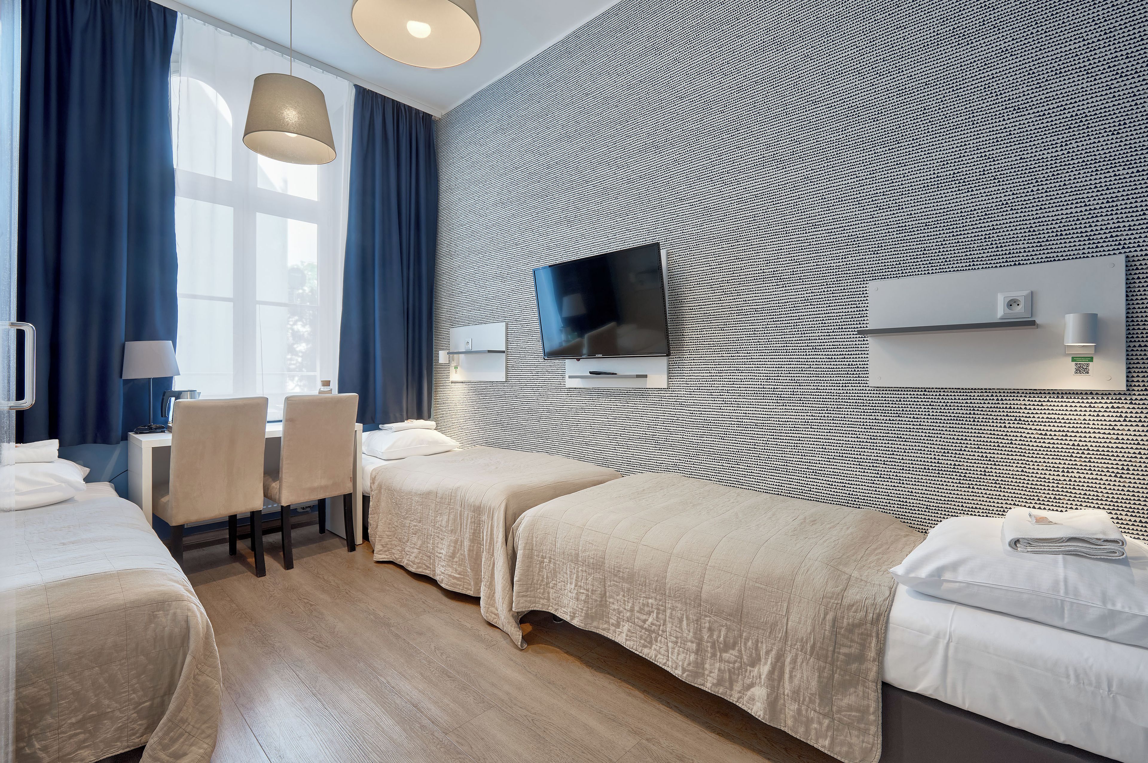 A hotel room with a bed, a desk, a chair, a TV, and a patterned wall.