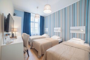 Ein Hotelzimmer mit zwei Betten, einem Schreibtisch mit Lampe, einem Fernseher und einer gestreiften Wand.