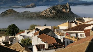 A coastal town with traditional architecture, including white buildings with red-tiled roofs, and a prominent rocky hill in the background. - Balcon del Velillos - Rincón de Marcelo (Moclin)