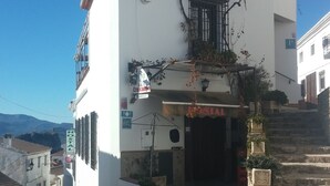 A white building with a balcony, a sign for a hostel, and a postal service entrance. - Balcon del Velillos - Rincón de Marcelo (Moclin)