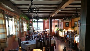 A restaurant with multiple tables set for dining, wooden beams on the ceiling, and potted plants. - Balcon del Velillos - Rincón de Marcelo (Moclin)